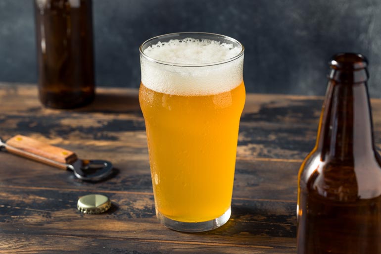 farmhouse ale glass with empty bottles and a bottle opener on tabletop