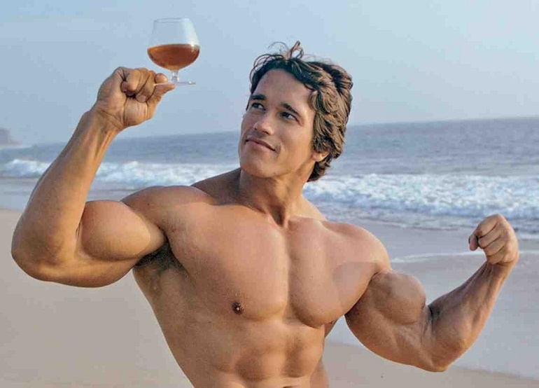 arnold schwarzenegger holding beer glass and flexing his copious muscles